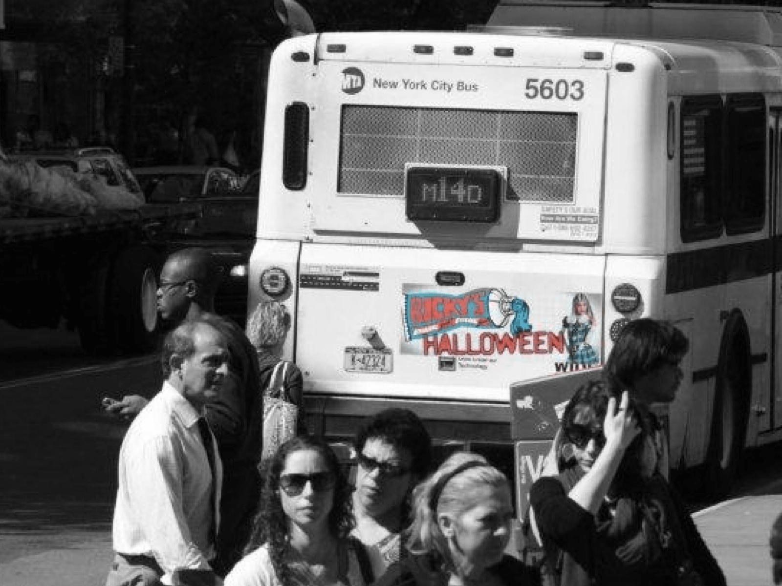 Ricky’s Halloween bus tail on a New York City bus with pedestrians crossing in Manhattan
